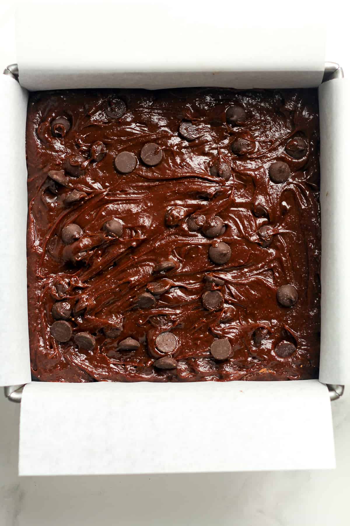 The brownie batter in a square pan with parchment paper.