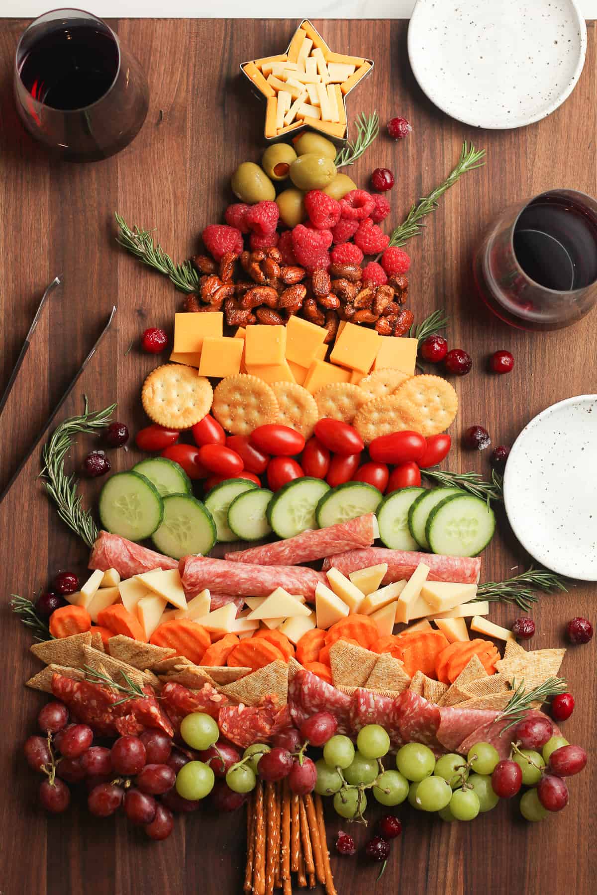 Overhead view of a Christmas Tree Charcuterie Board with small plates and glasses of wine.