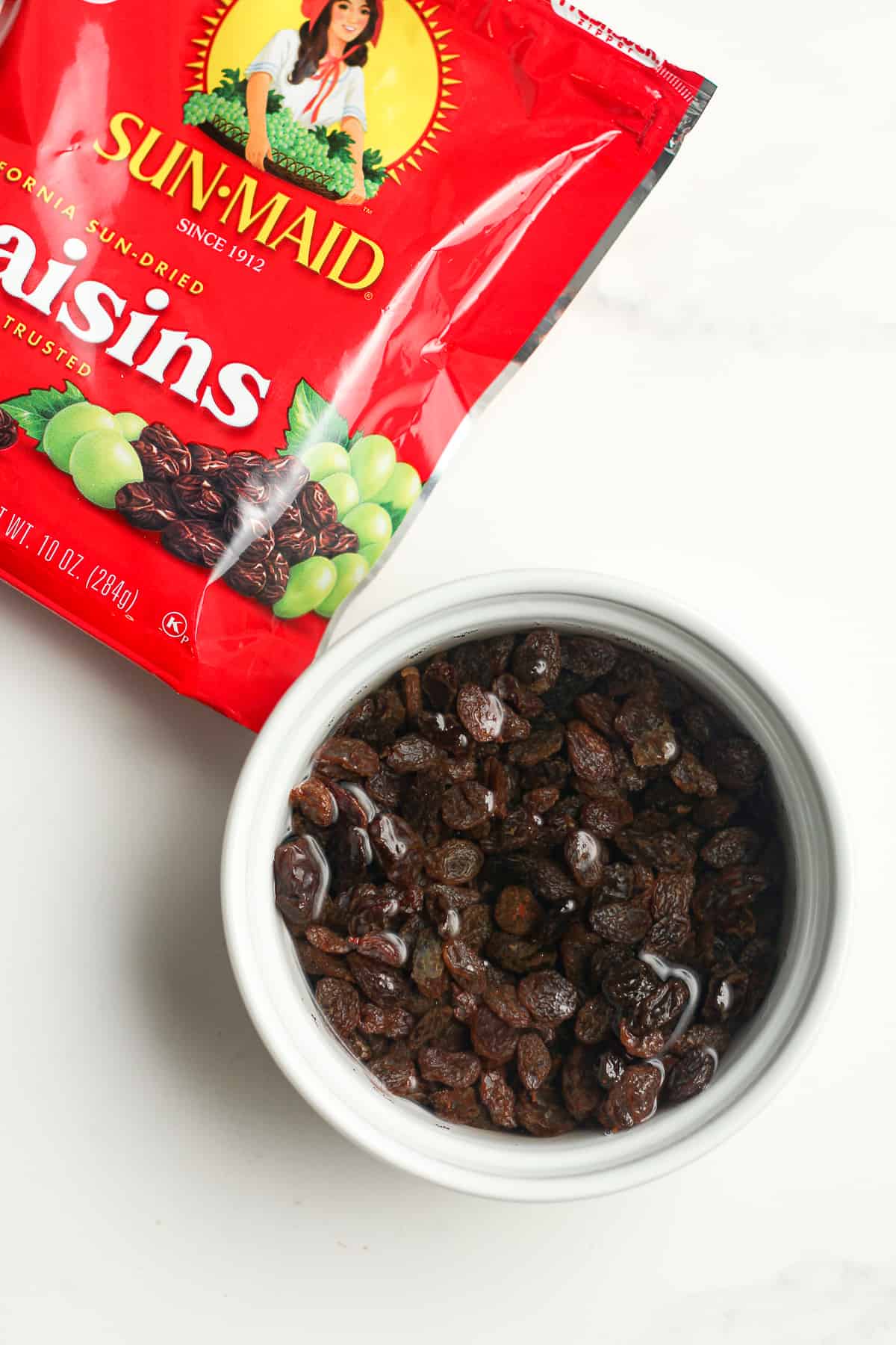 A bowl of the soaked raisins with a package next to it.