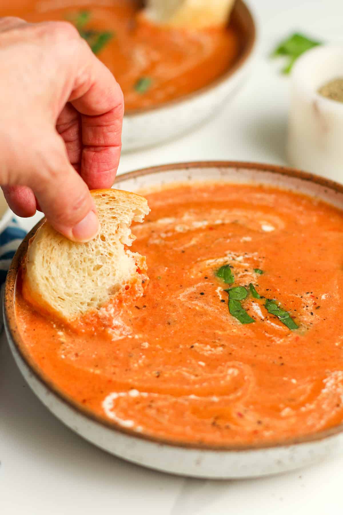 My hand dipping some bread into a bowl of creamy tomato bisque.