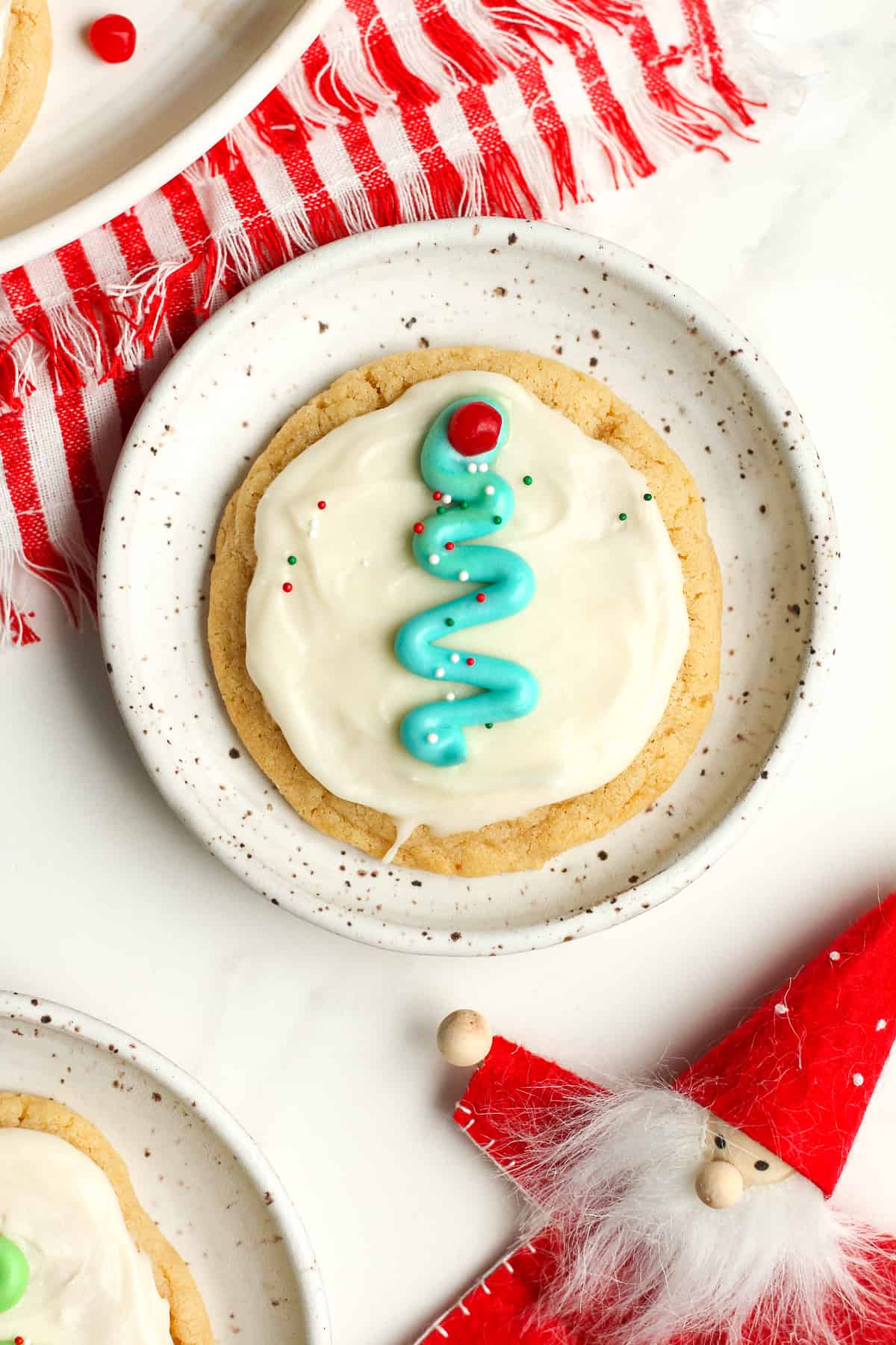 A plate with a single frosted sugar cookie next to an ornament.