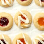 Closeup of jam thumbprint cookies on white parchment paper.