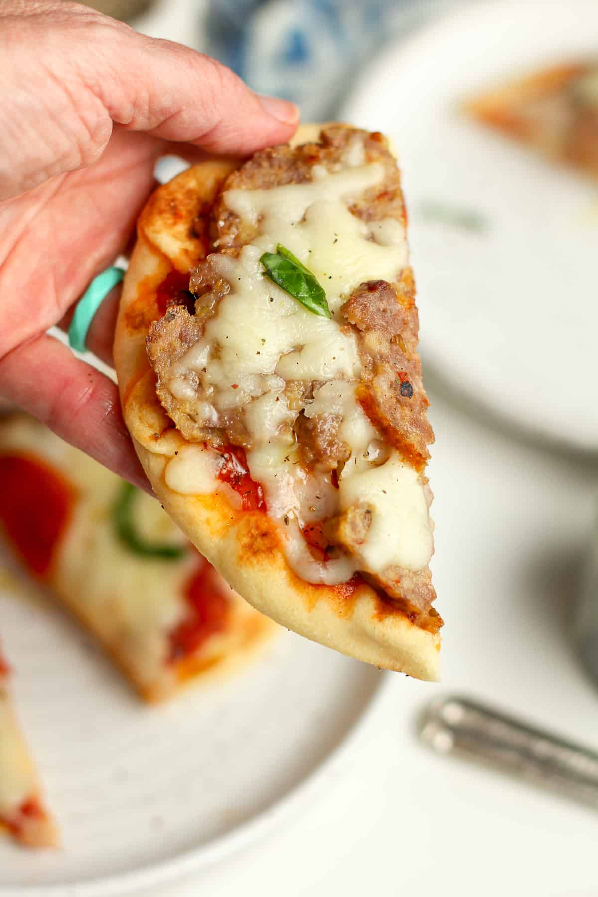 A hand holding a slice of the sausage pizza.