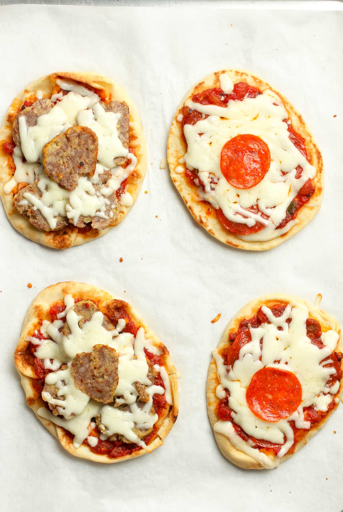 Baked naan bread pizza with sausage and pepperoni toppings.