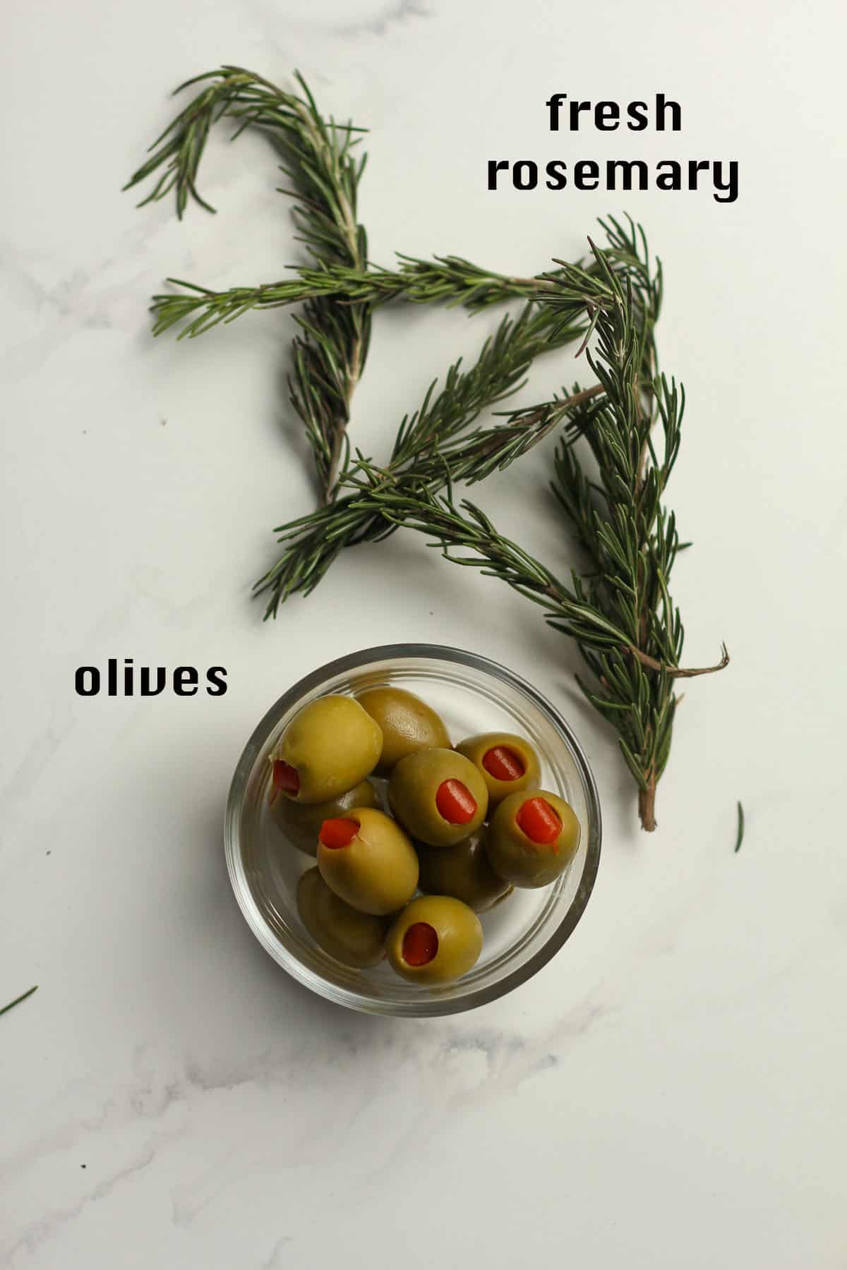 A bowl of green olives plus some fresh rosemary.