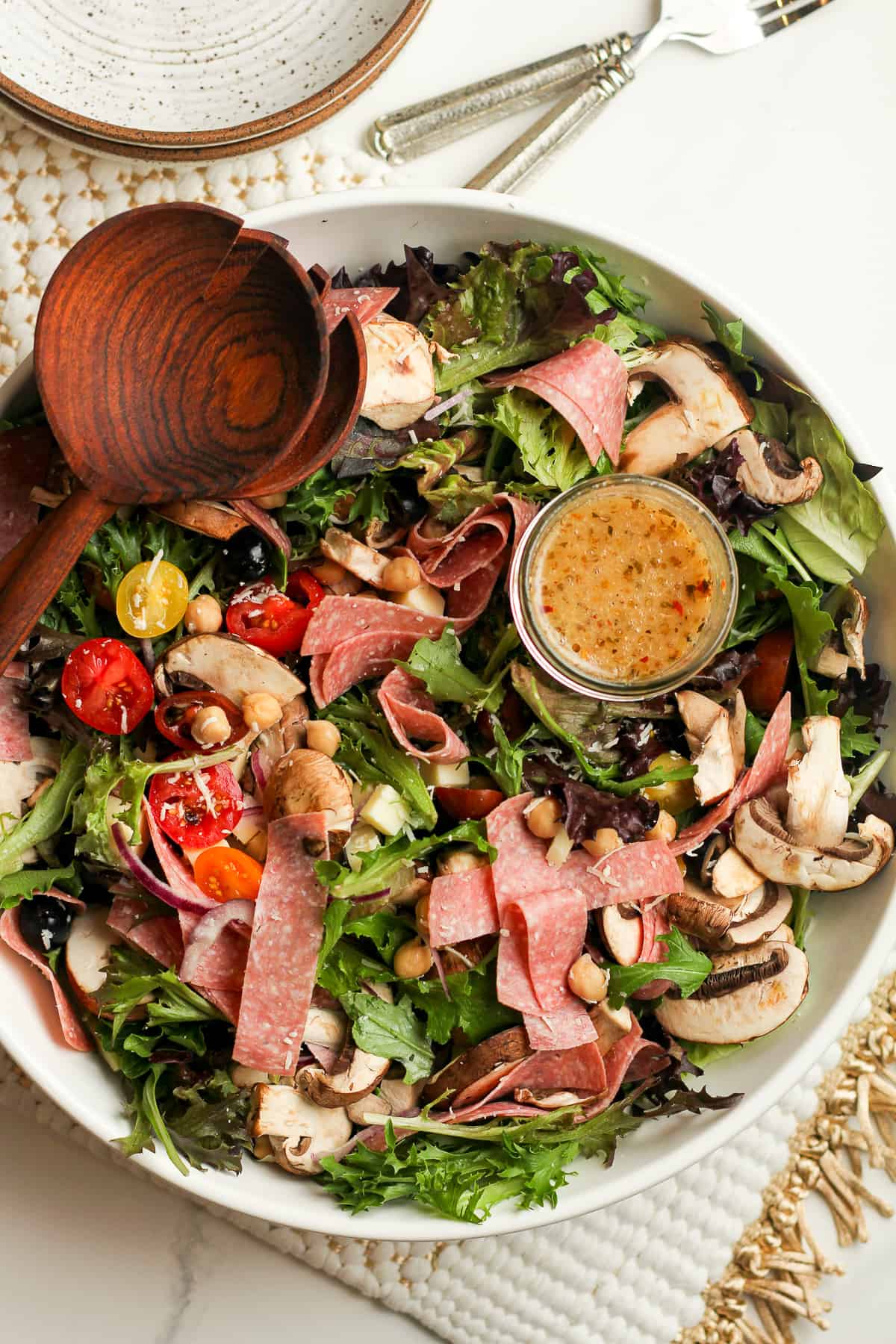 A large Italian salad mixed together with wooden salad spoons.