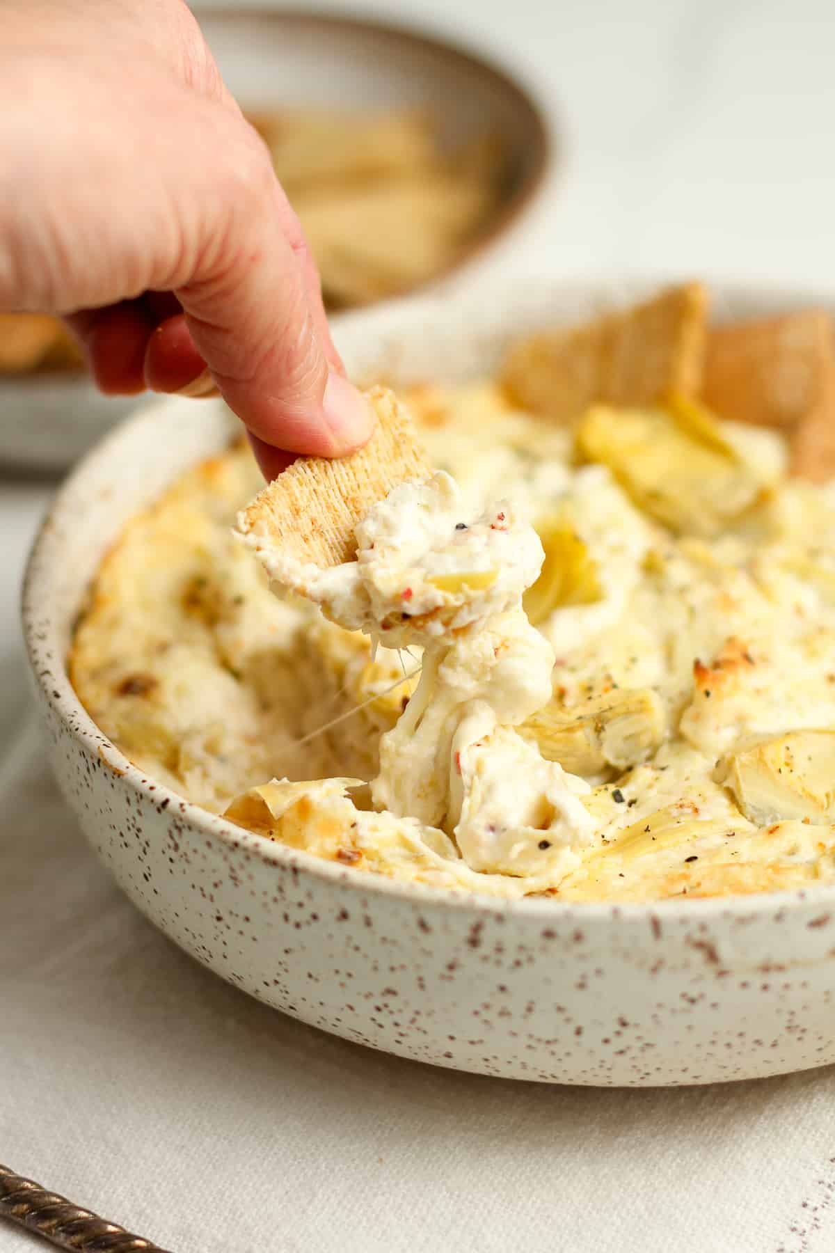 Side shot of a bowl of the dip with a hand dipping a cracker inside.