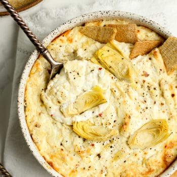 A bowl of baked artichoke dip with a serving spoon.