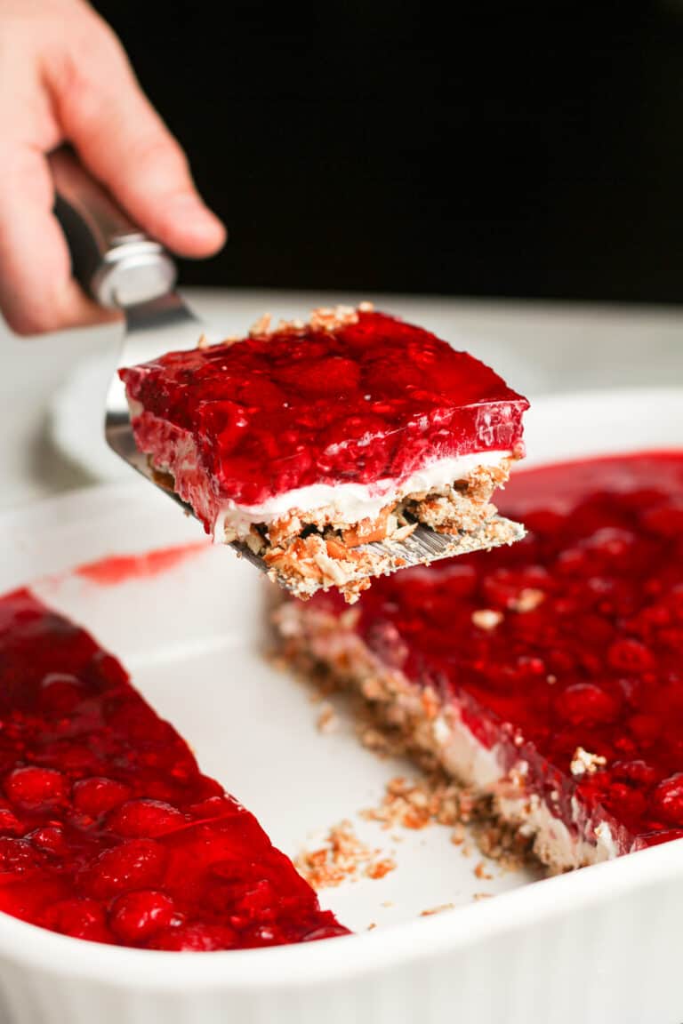 A hand serving a piece of fruit pretzel salad.