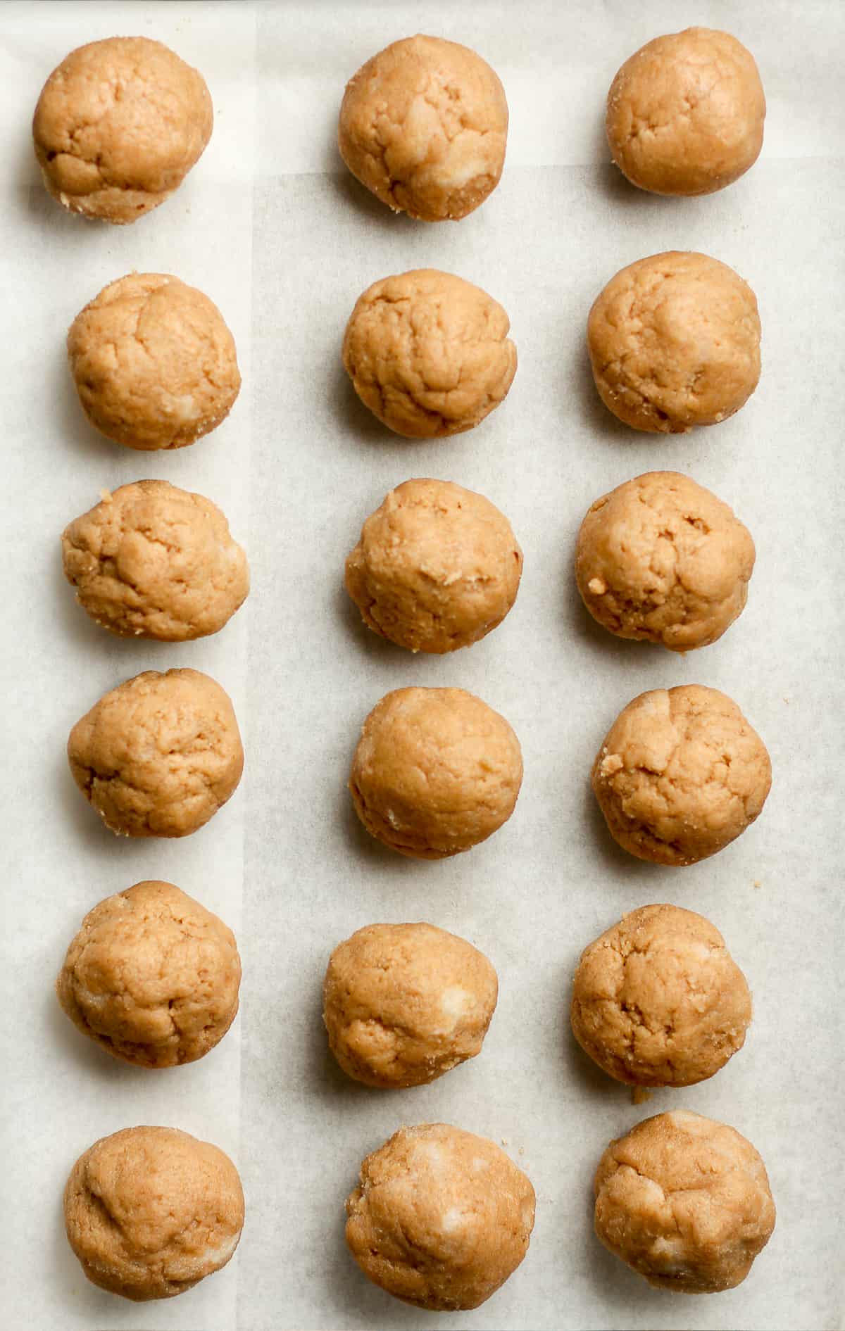 18 snickerdoodle cookie balls on white parchment paper.