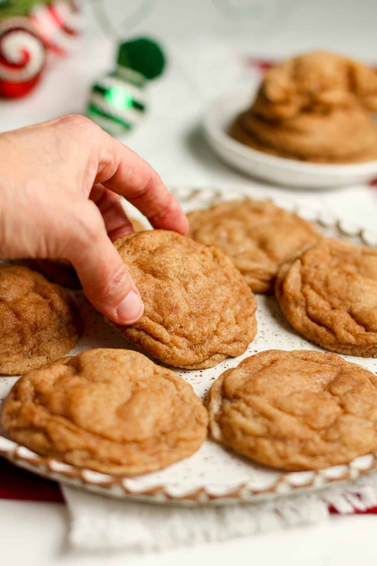 Side view of a plate of snickerdoodle cookies, with a hand lifting one up.
