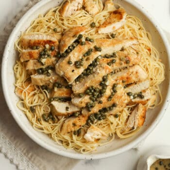 A bowl of pasta with sliced chicken and a caper lemon sauce.