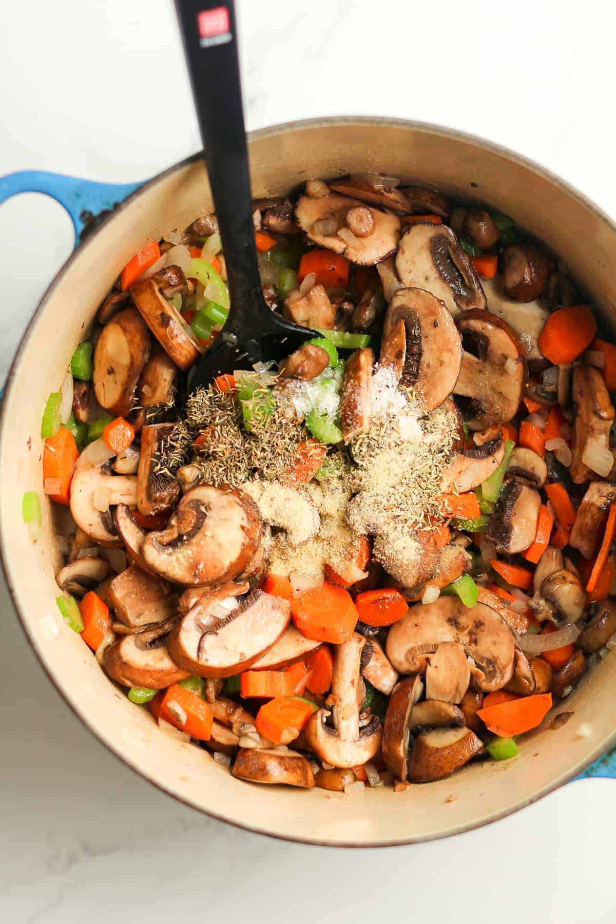 A stock pot of cooked veggies with seasonings on top.