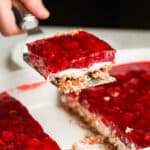 A hand dishing out a piece of raspberry pretzel salad with a spatula.