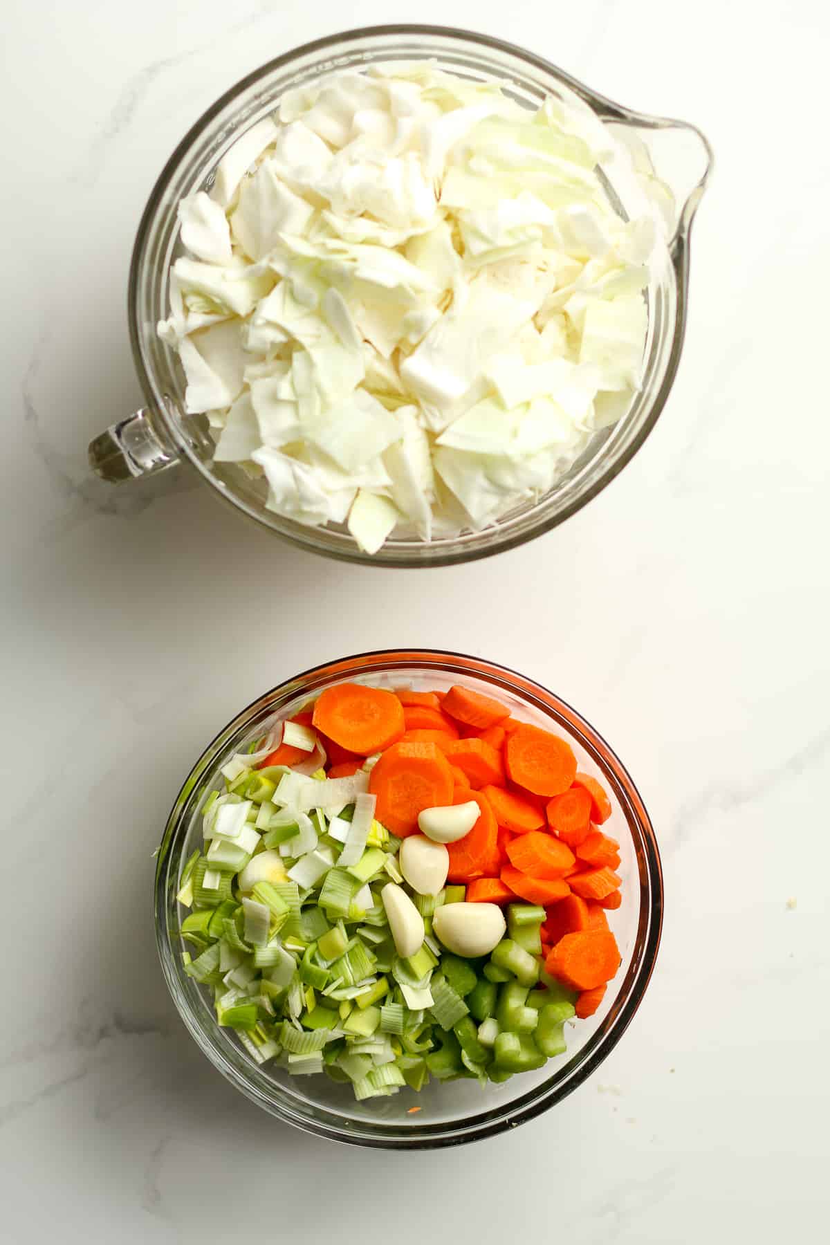 A large measuring cup of chopped cabbage plus a bowl of chopped leek, carrots, celery, and garlic.