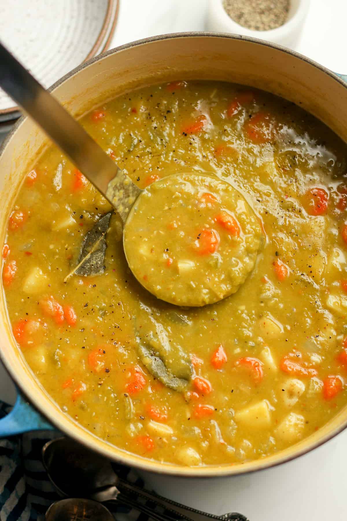 A soup ladle lifting up some split pea vegetable soup.