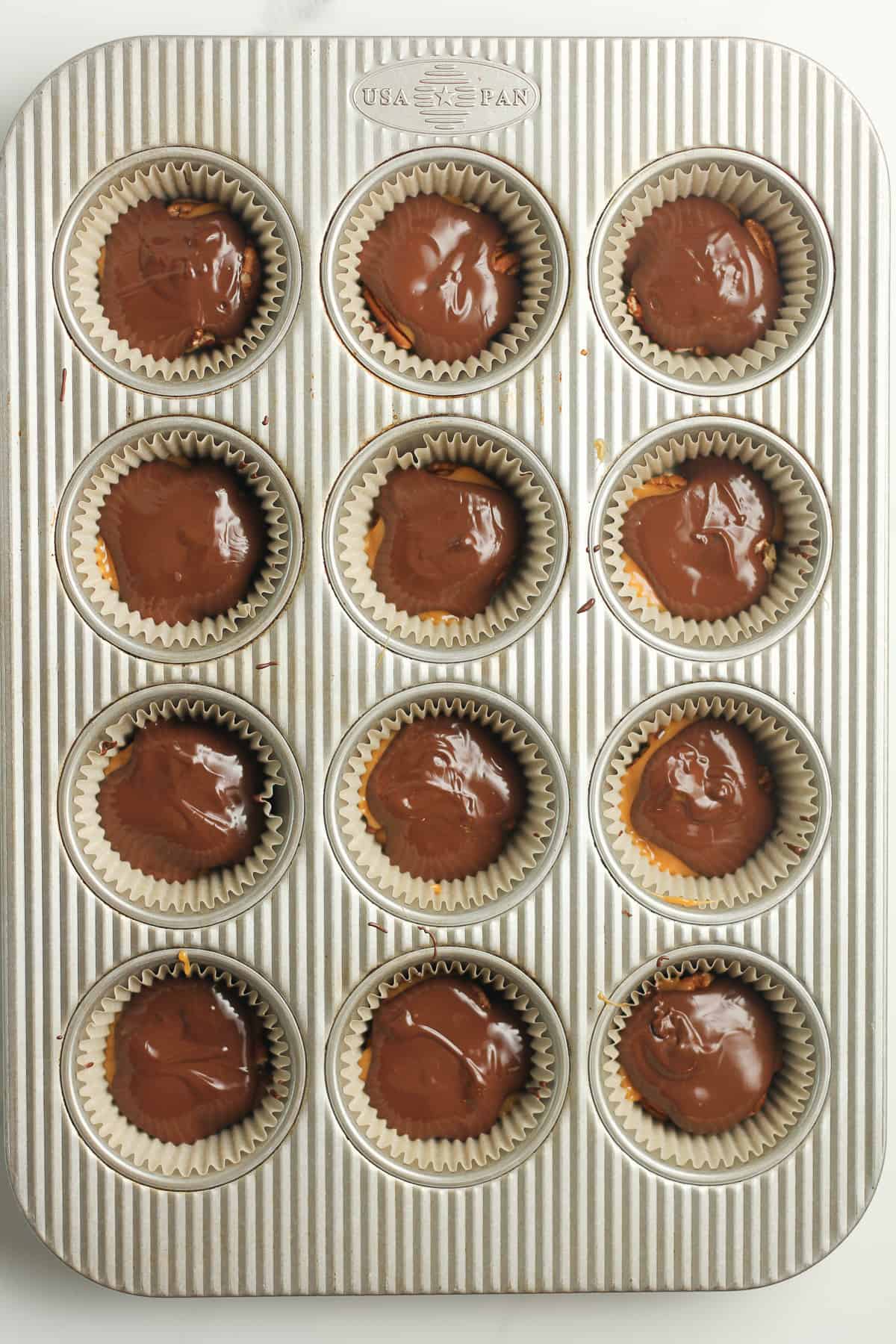 A 12-cup muffin tin with chocolate turtles in parchment liners.