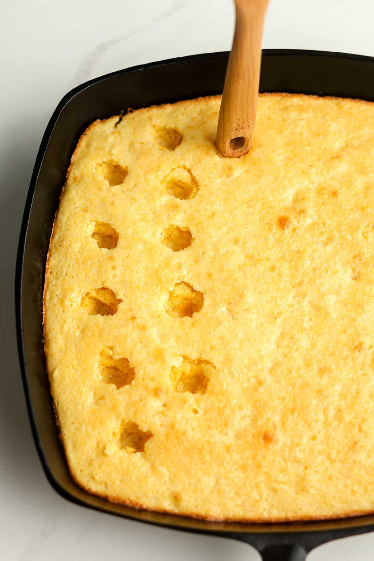 A skillet of cornbread with holes poked on top.