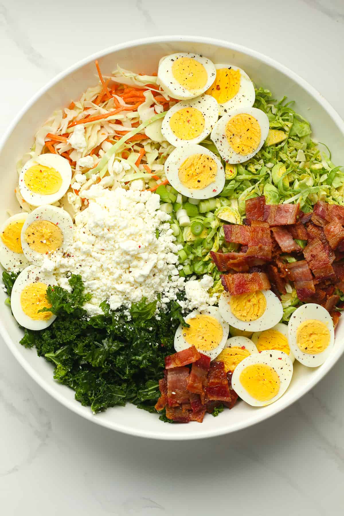 A large bowl of the salad with the eggs, bacon, and goat cheese on top.