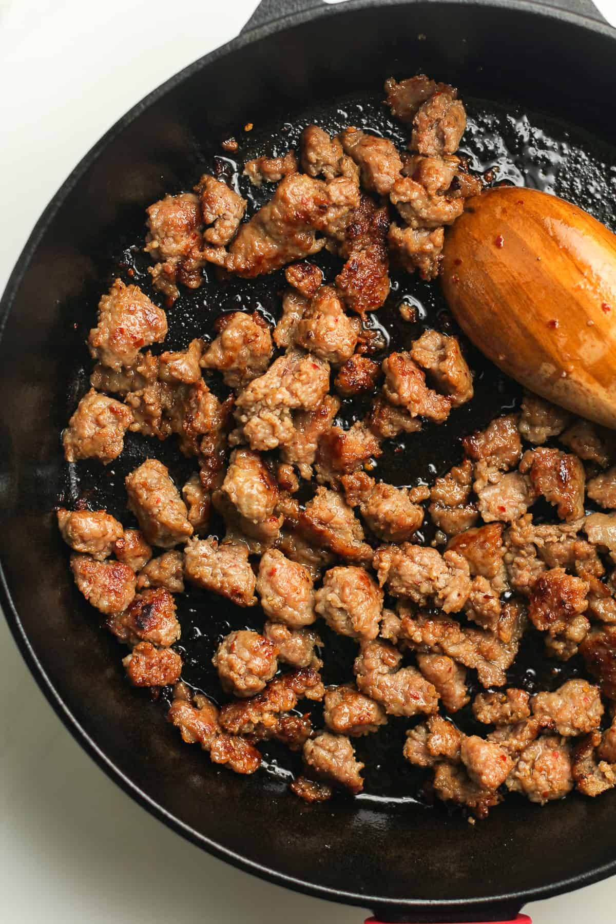 The skillet of cooked sausage with a wooden spoon.
