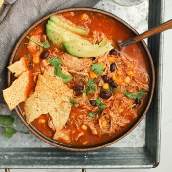 A closeup on a bowl of chicken tortilla soup with avocado and chips.