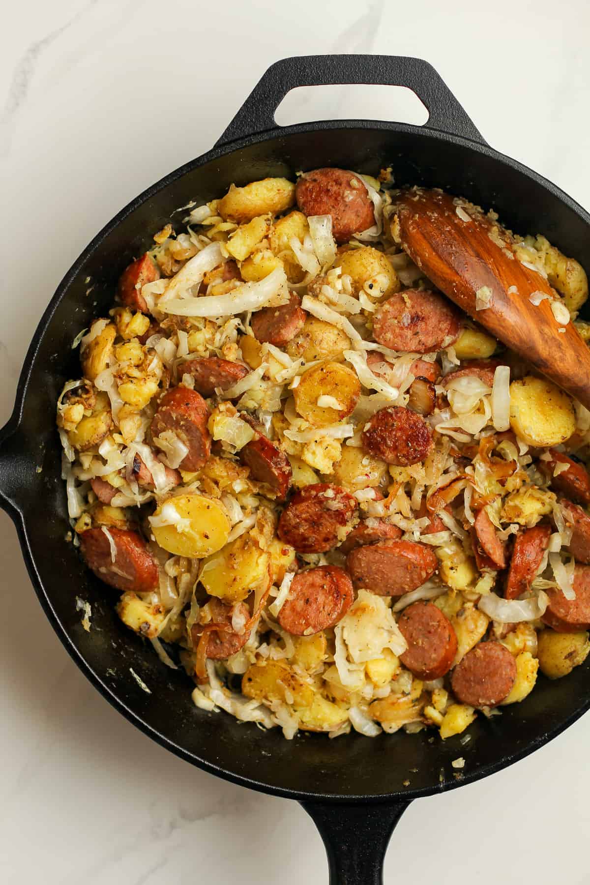 Overhead shot of the kielbasa and sauerkraut skillet with a wooden spoon.