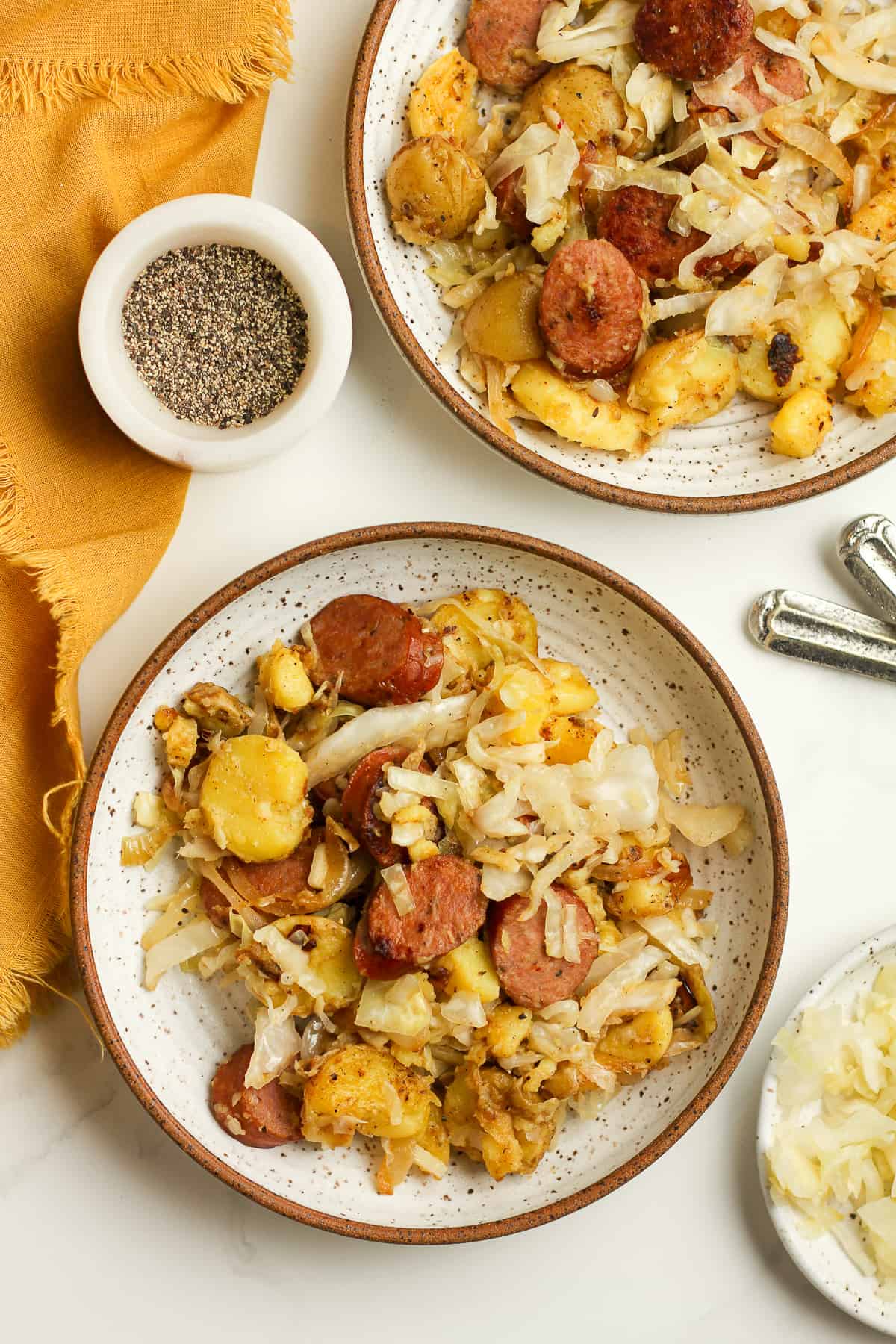 Two bowls of kielbasa, sauerkraut, and potatoes.