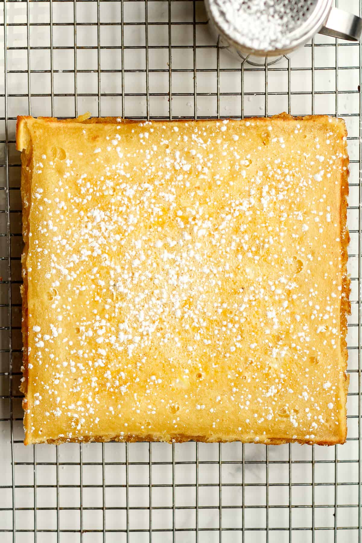 A cooling rack of the square lemon bars with powdered sugar.