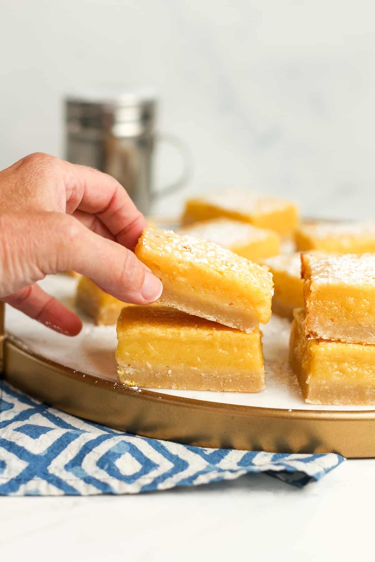 A hand lifting a lemon bar off of a white tray.
