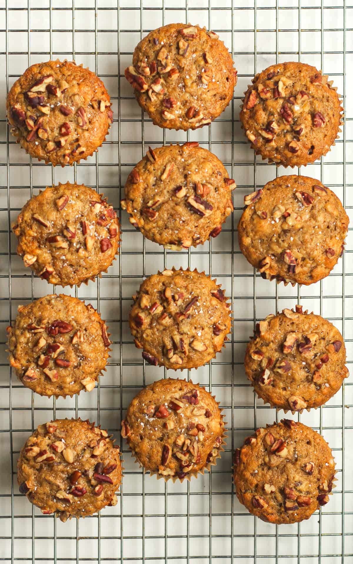 A cooling rack with baked banana muffins with pecans on top.