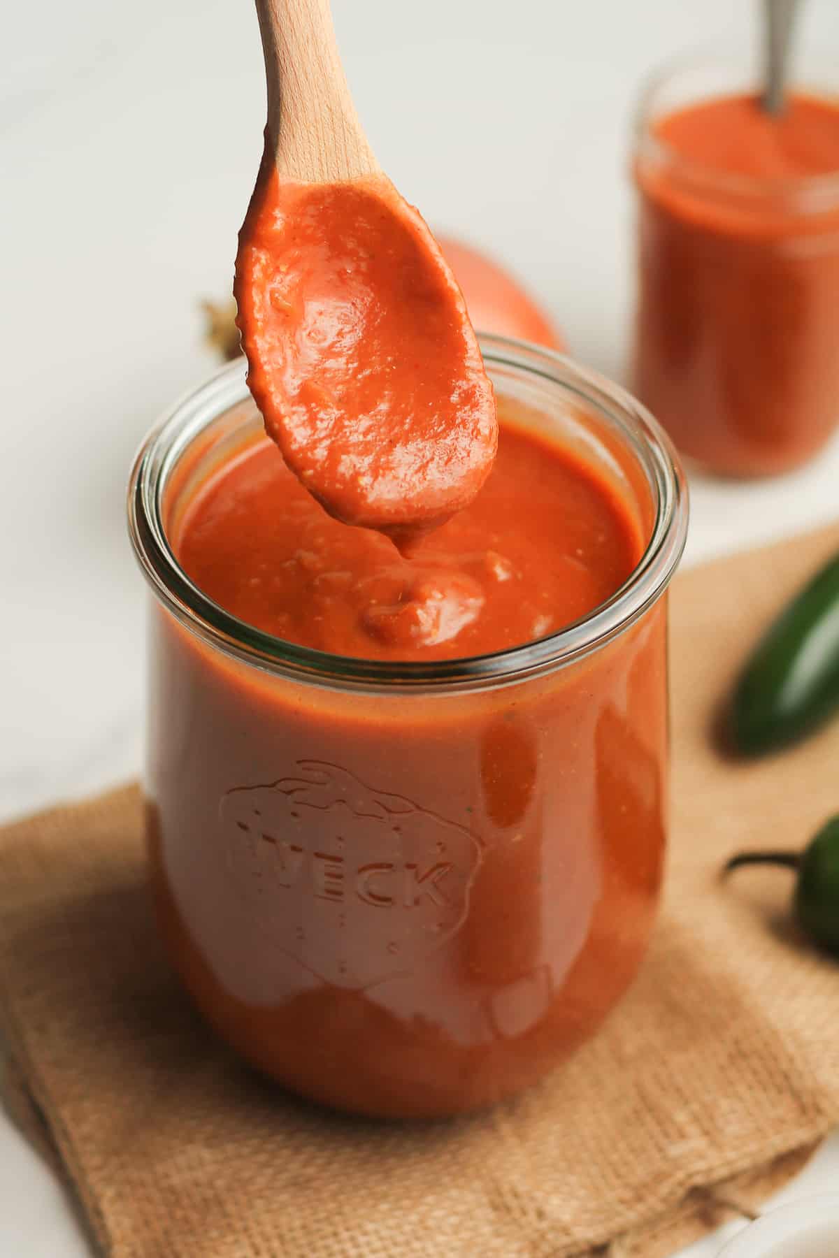 A spoonful of enchilada sauce dripping into a large jar of sauce.