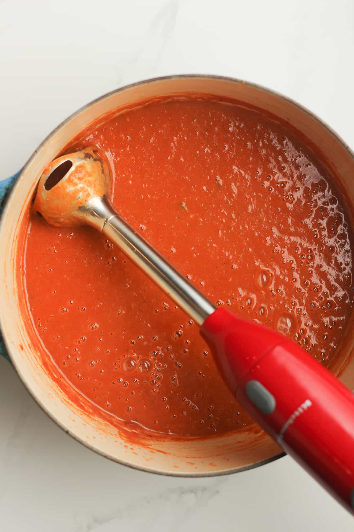 An immersion blender in a large pot of sauce.