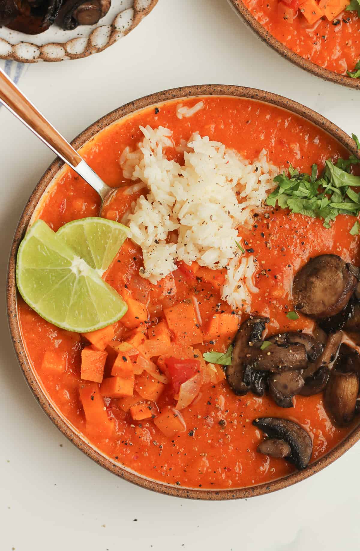 Closeup on a bowl of sweet potato red curry soup, with rice and mushrooms.