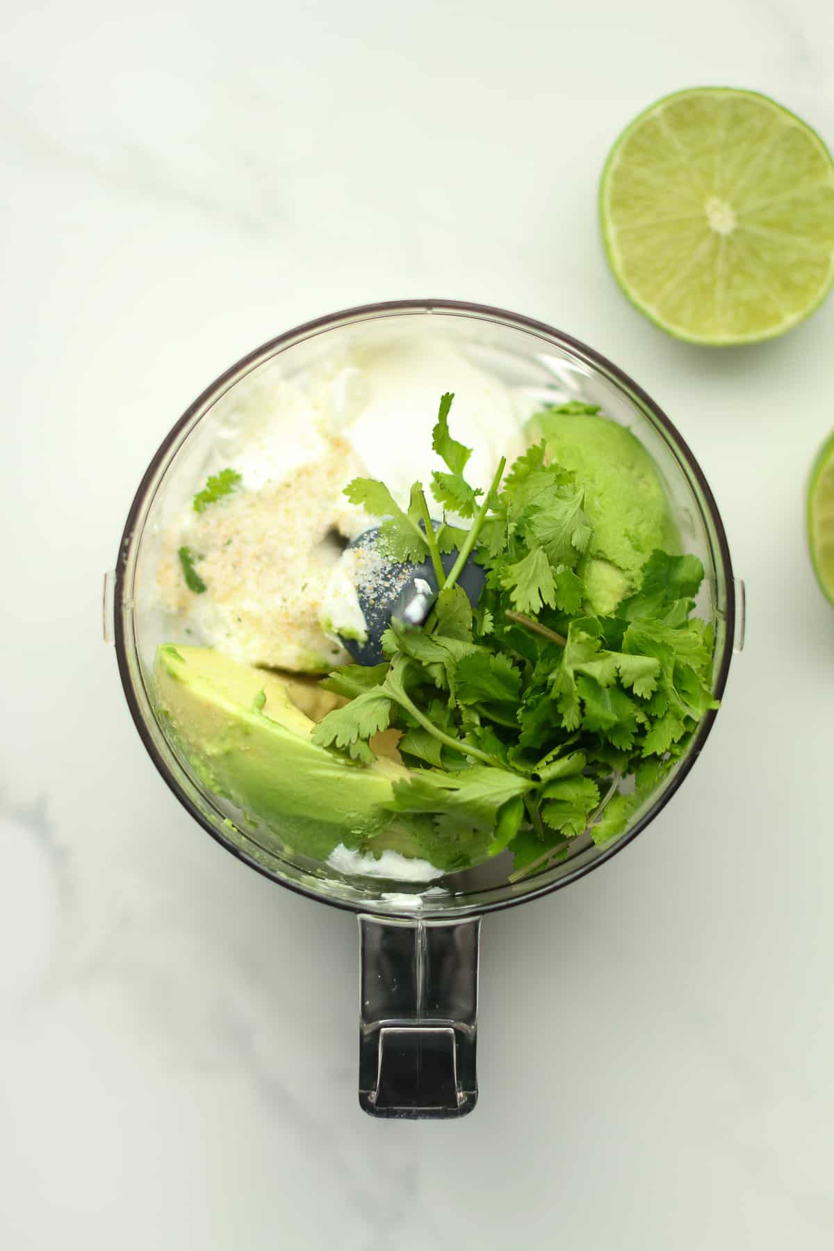 A food processor filled with the Avocado Crema ingredients with limes beside it.