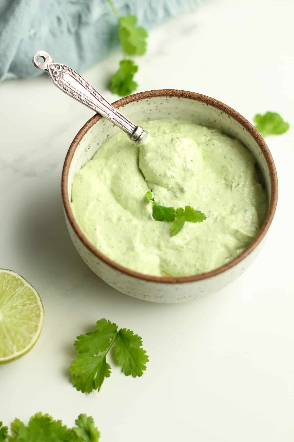 Side view of a bowl of avocado crema with a teaspoon inside.