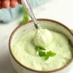 A hand holding a spoonful of avocado crema overt small bowl.