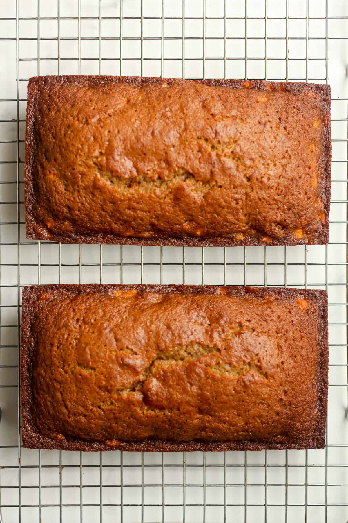 Two loafs of carrot cake bread on a cooling rack.