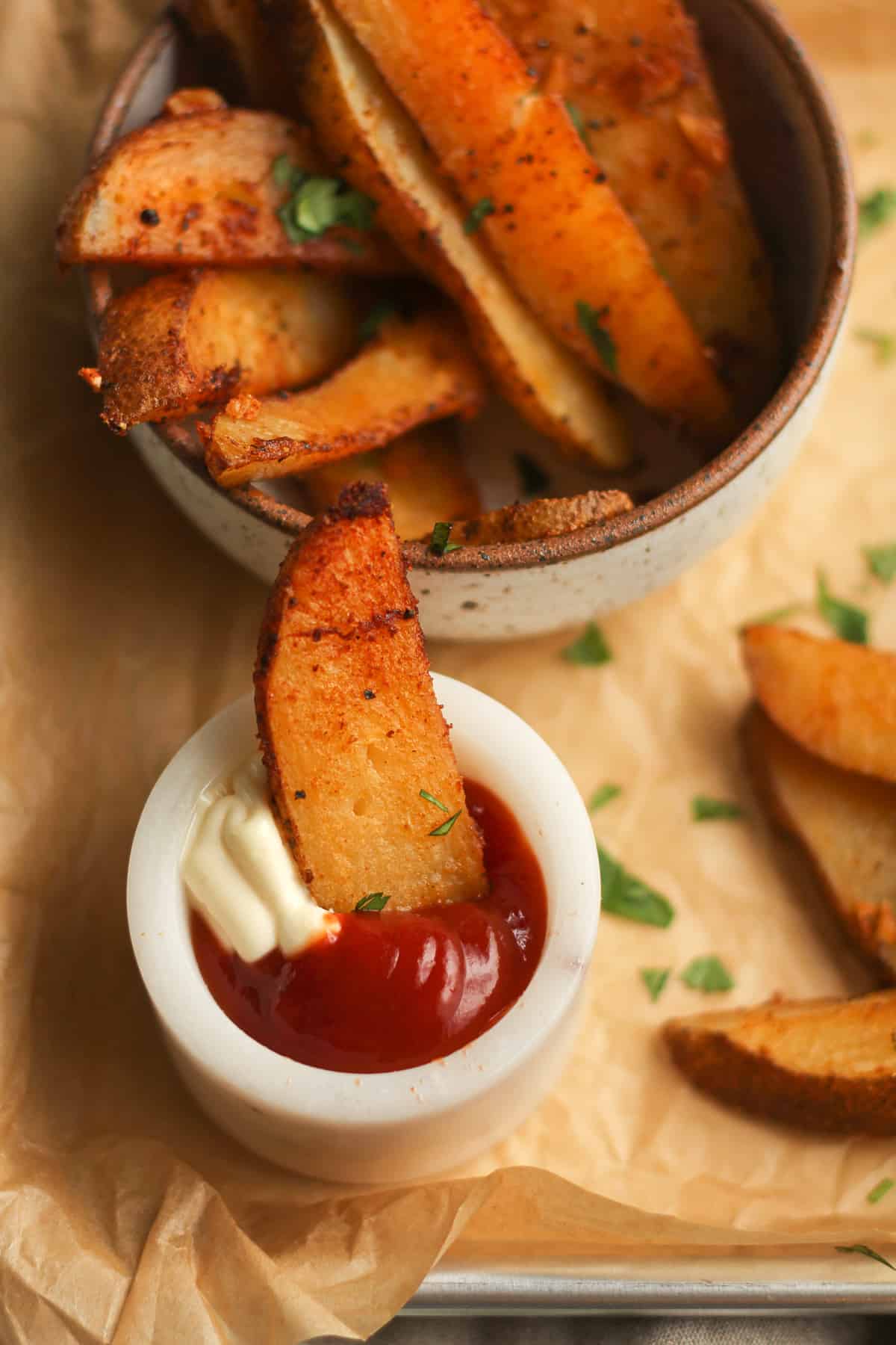 Side shot of a baked fries in a small bowl of ketchup and mayo, with a bowl of fries in back of it.
