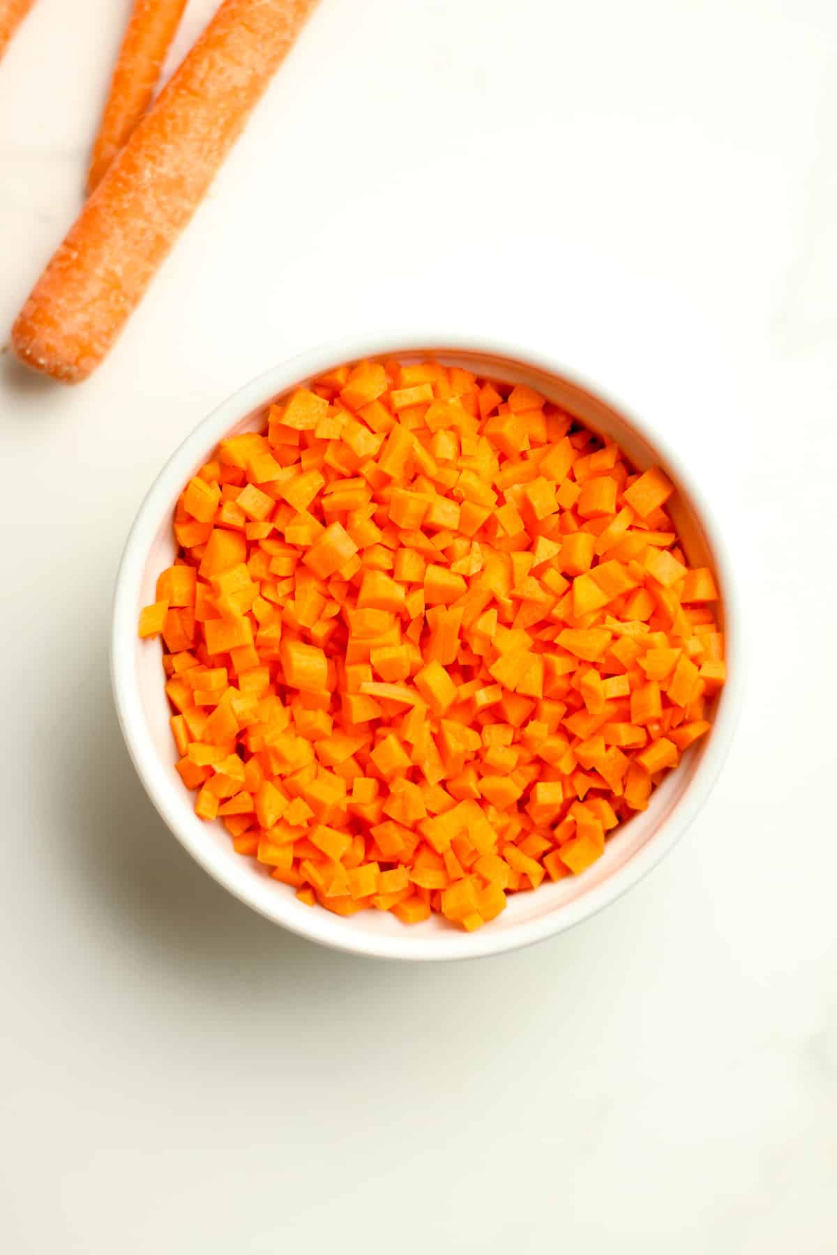 A small bowl of diced carrots with carrot sticks.