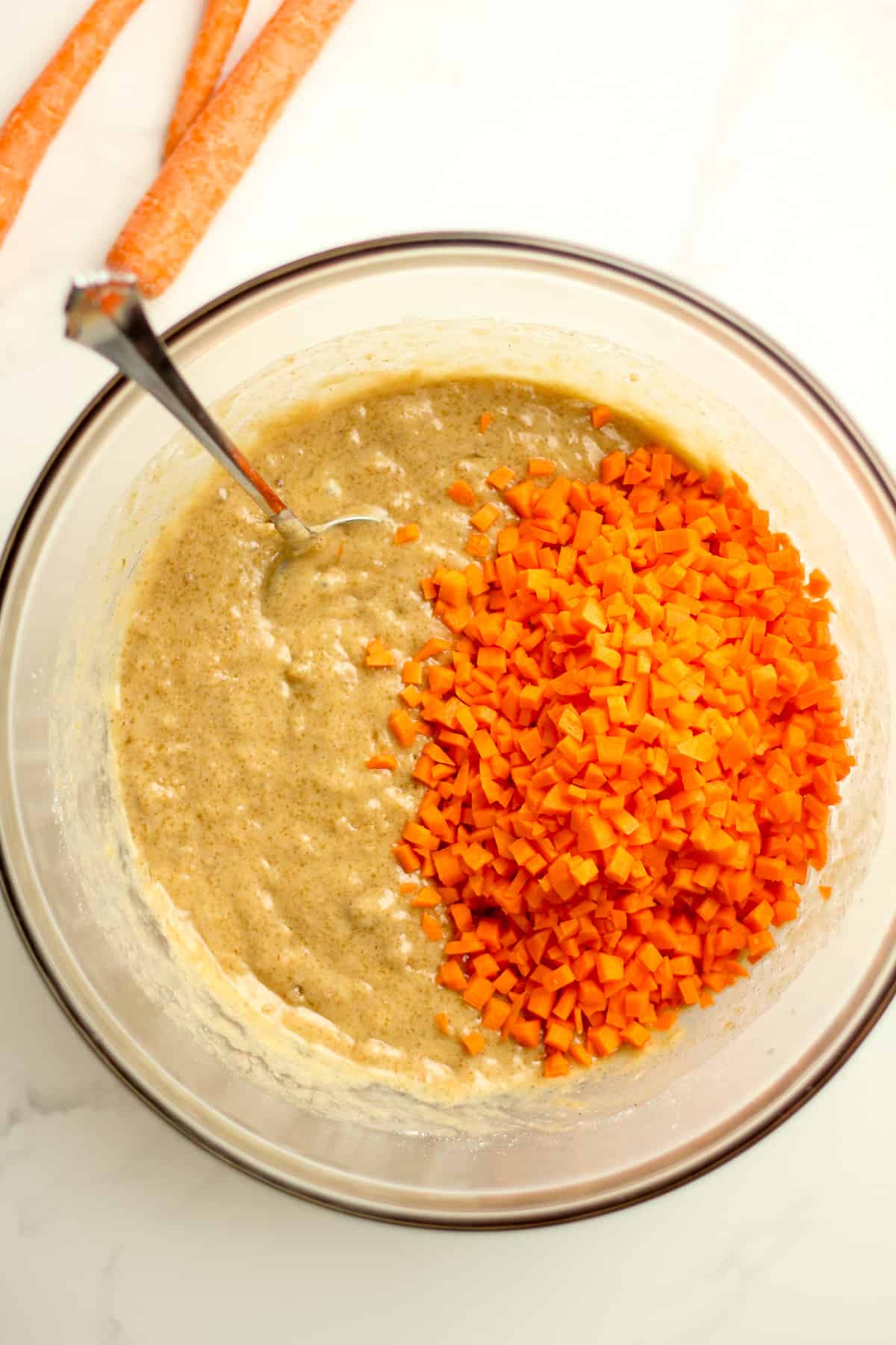 A bowl of the carrot cake batter with the diced carrots, with a spoon.