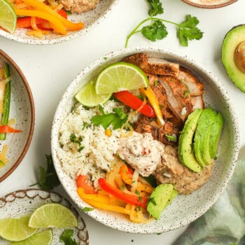 A chicken fajita bowl with grilled peppers and onions, rice, beans, and avocado slices.