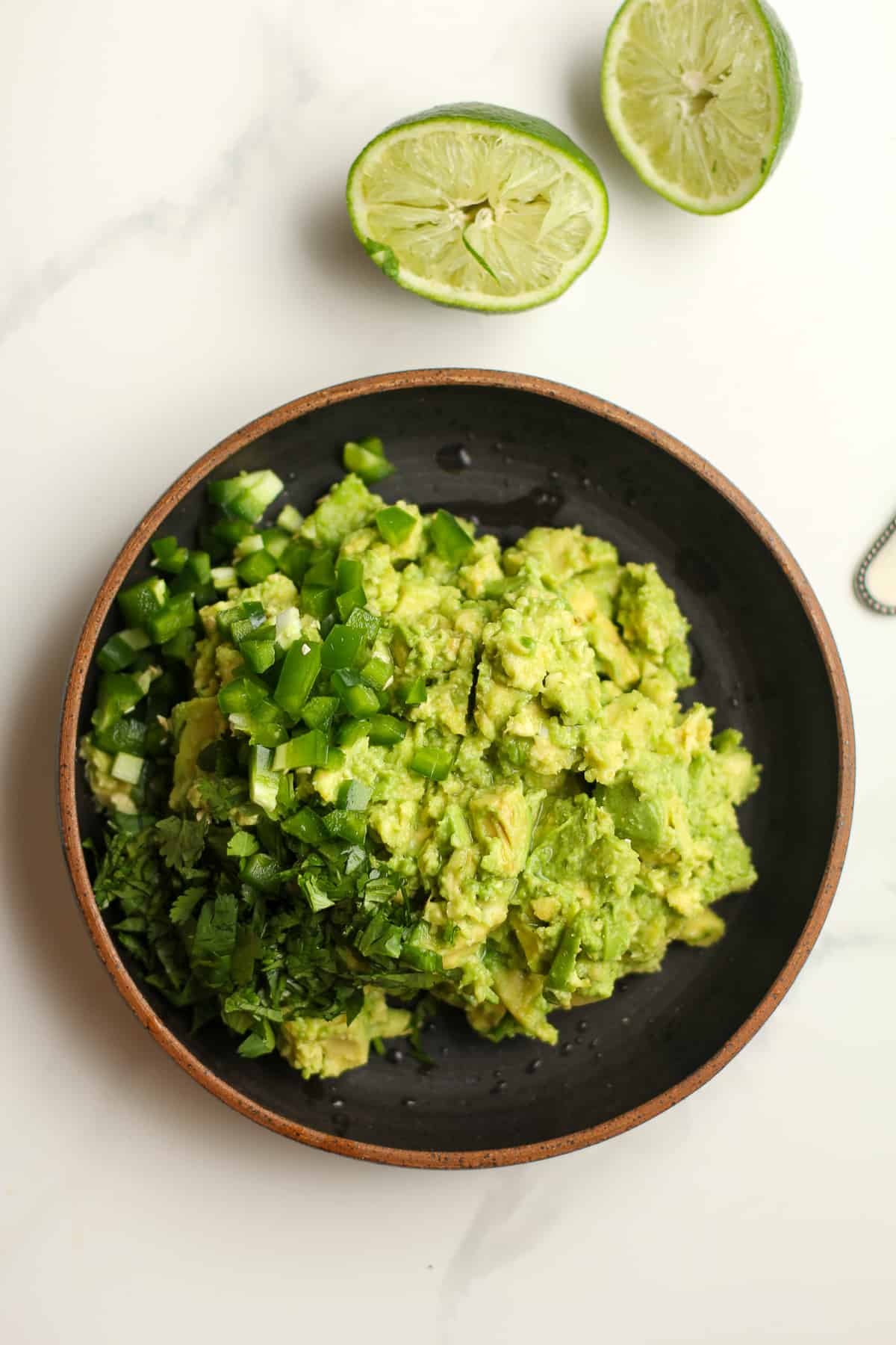 A black bowl of the chunky avocado with jalapeño and cilantro on top.