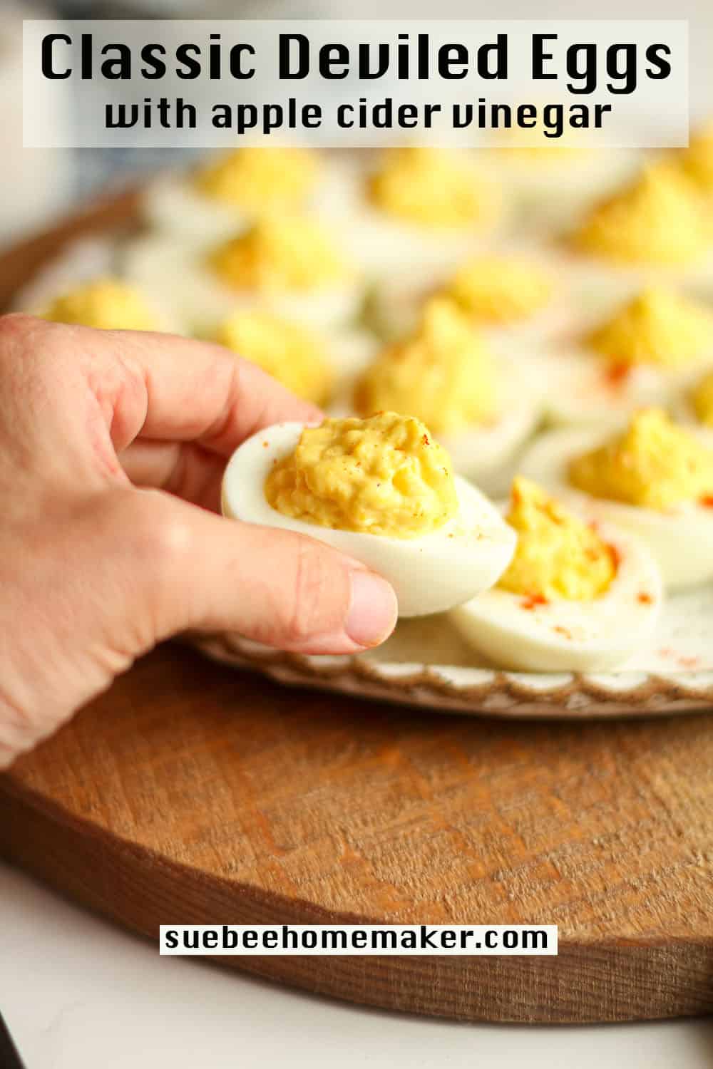 My hand reaching for a deviled egg above a plate of eggs.
