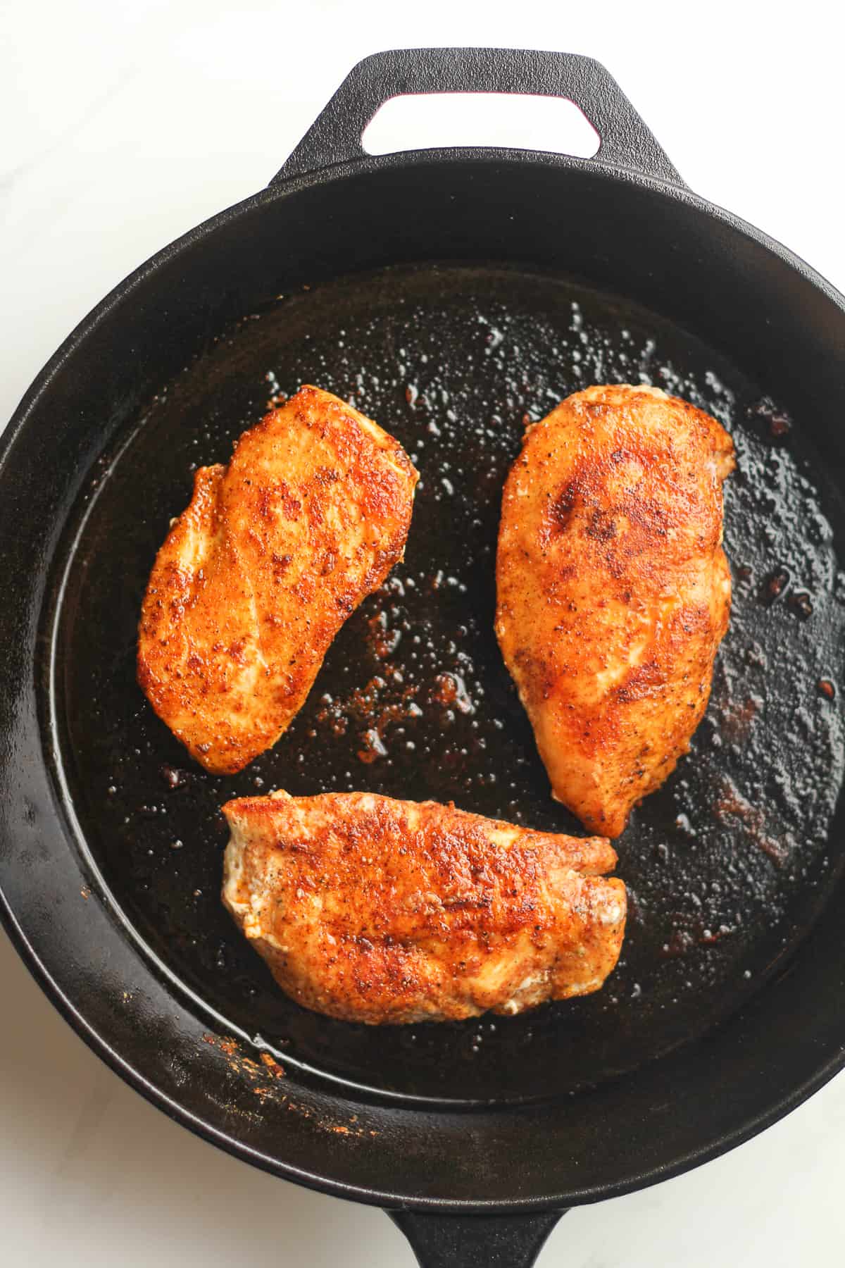 A skillet with three seared chicken breasts.