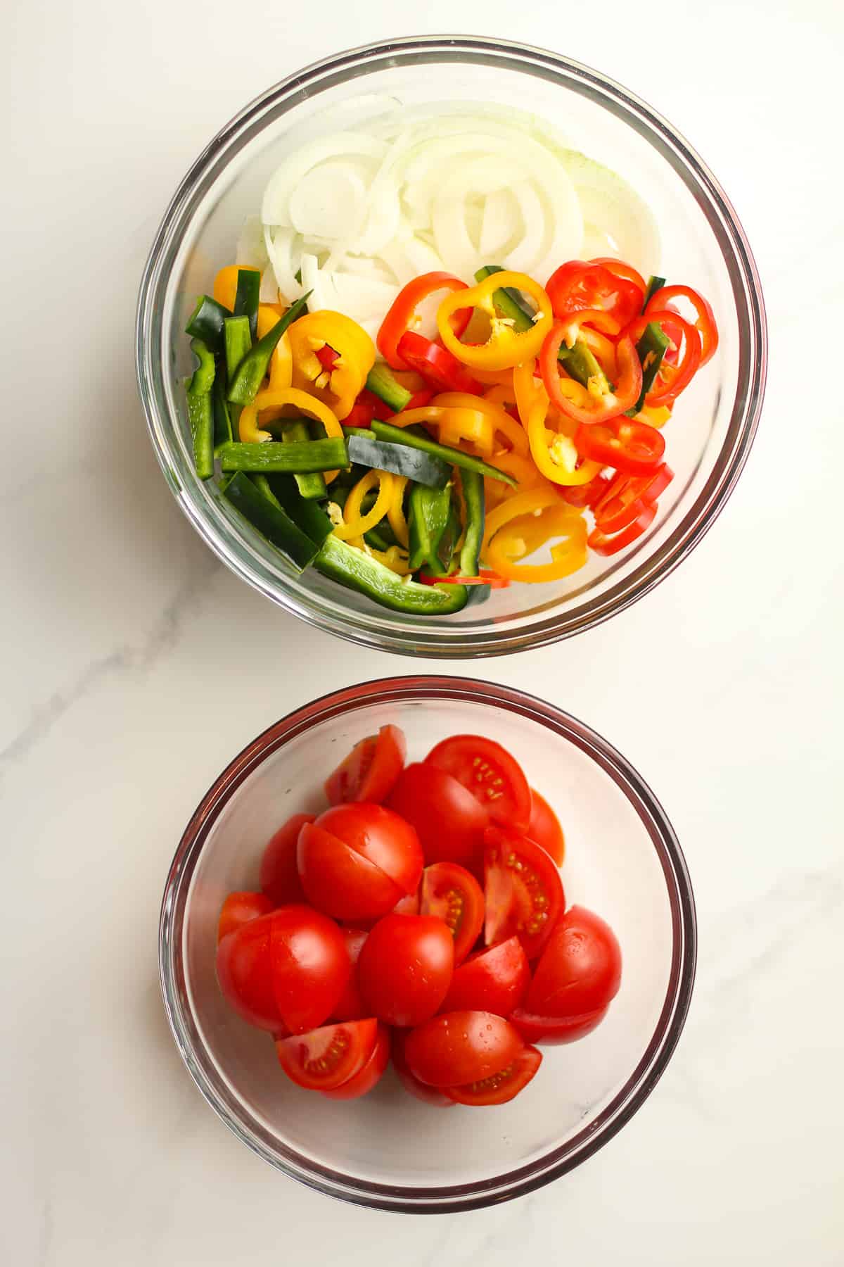 A bowl of the sliced peppers and onions, and another bowl of the chopped tomatoes.