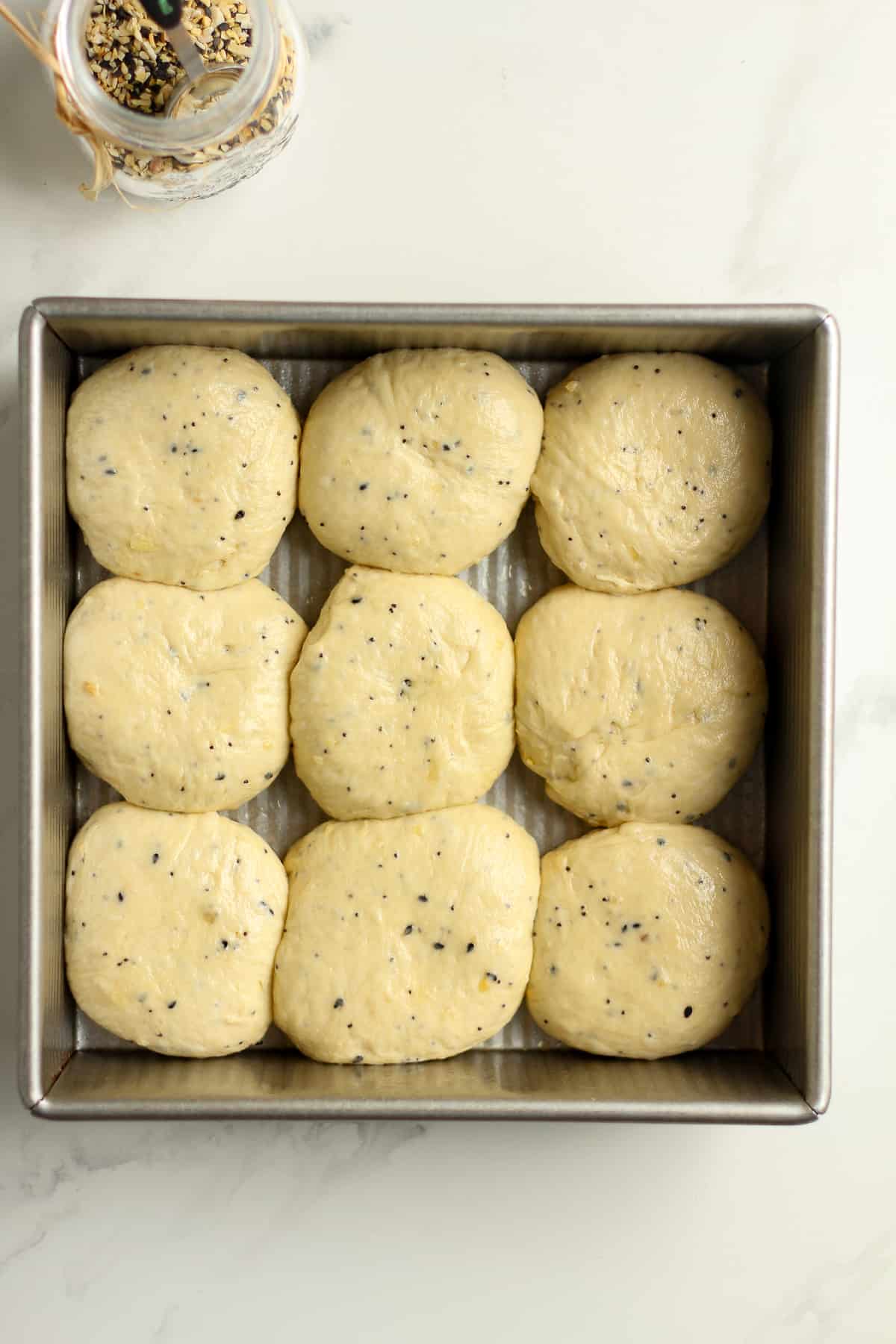 A square pan with nine dinner rolls before baking.