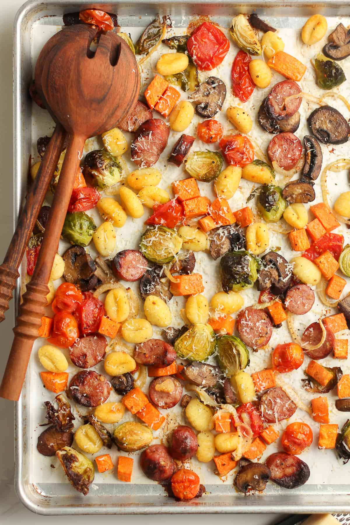 A sheet pan of the gnocchi bake with parmesan cheese on top, and two wooden spoons.