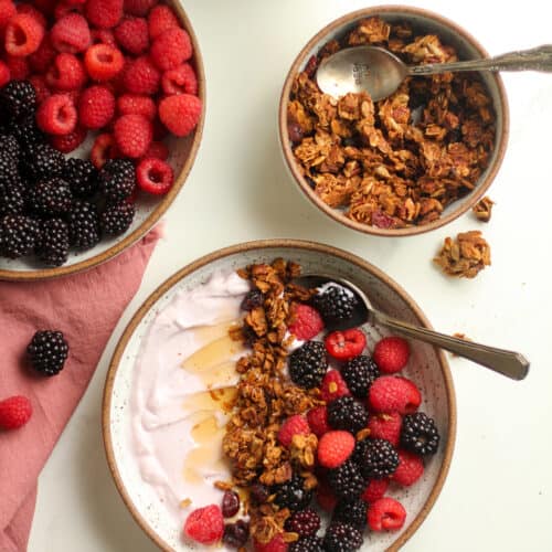 Overhead shot of a bowl of yogurt, granola, and fruit, with a vas of flowers next to it.