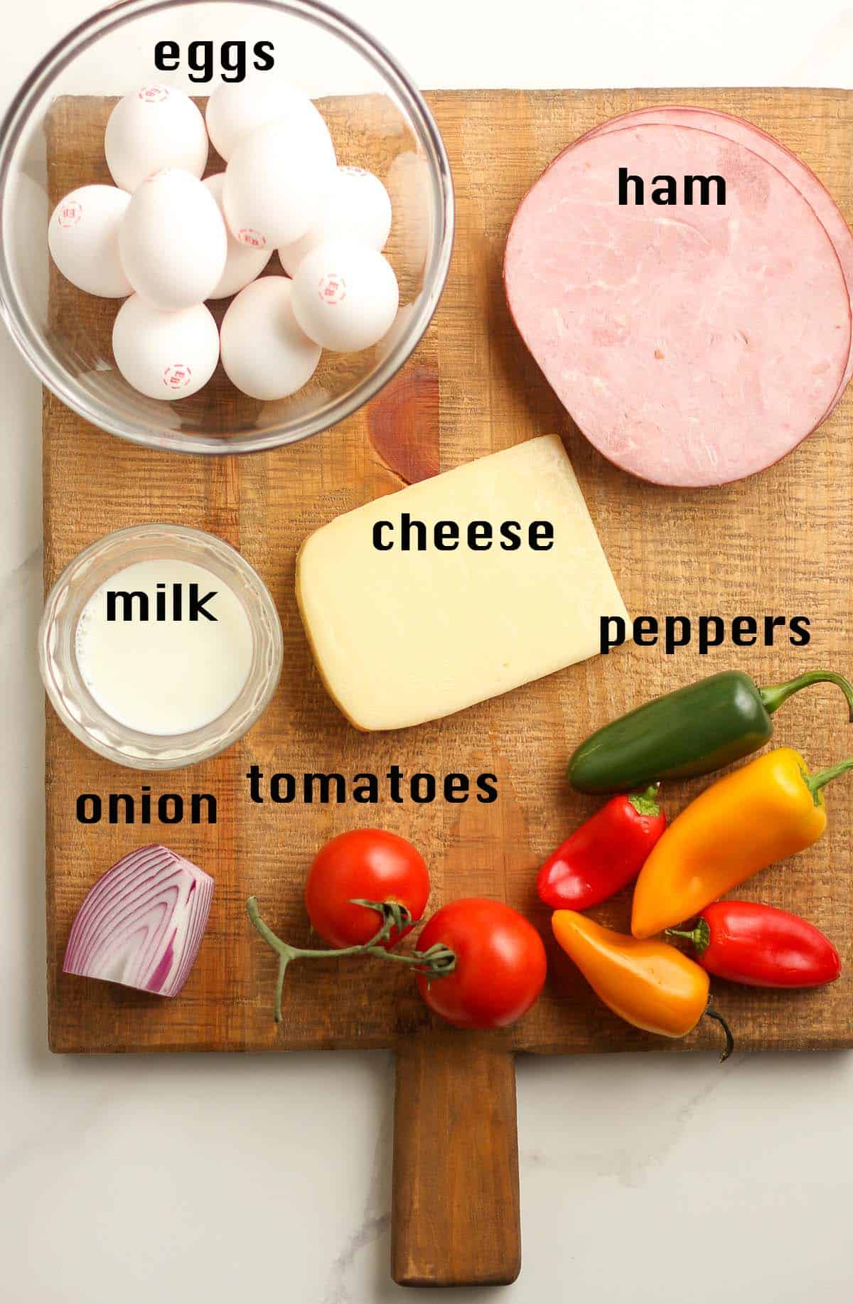 A wooden board with the labeled ingredients, including ham, cheese, eggs, and veggies.