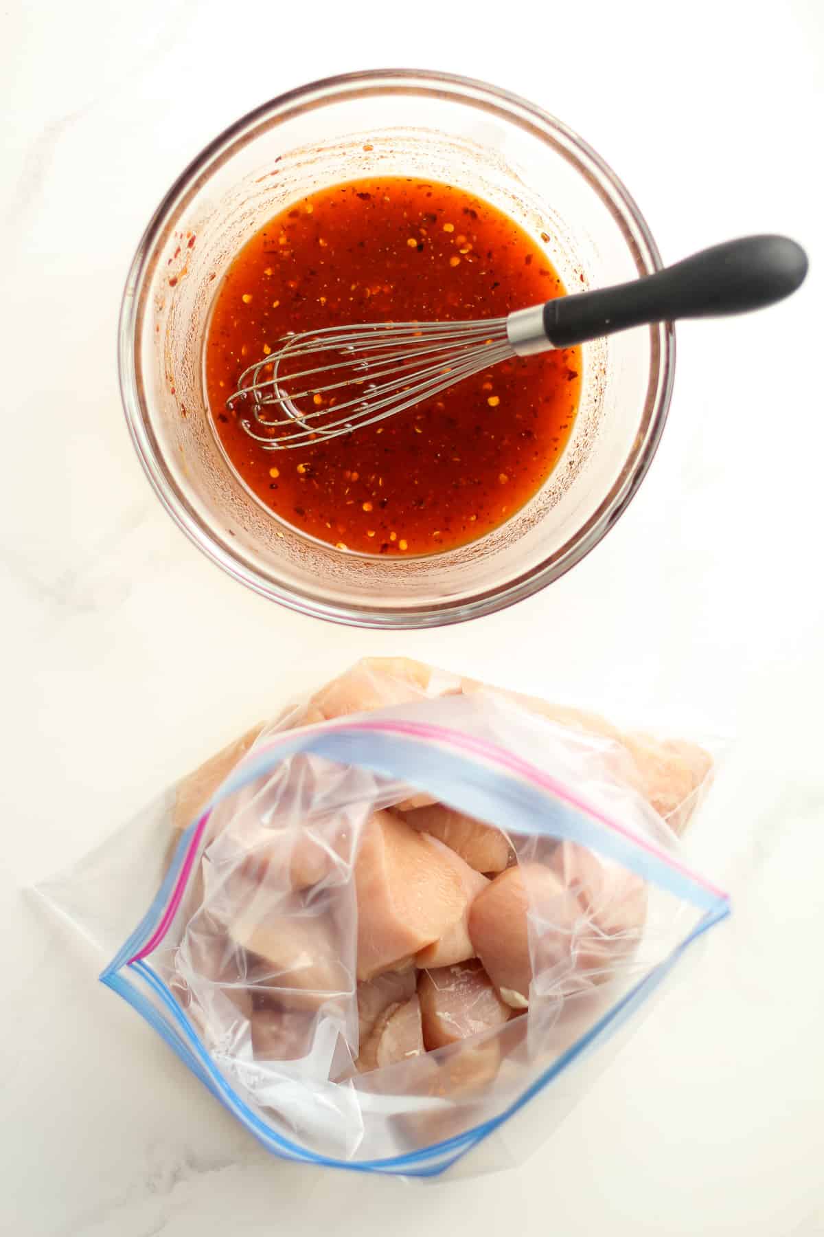 A bowl of the honey sriracha sauce next to a bag of chicken breasts, cubed.